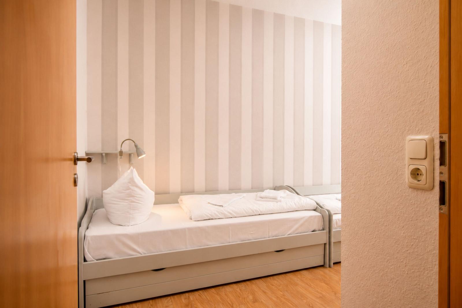 Schlafzimmer mit Bett, Kissen und Streifenwand. Tür und Steckdose sichtbar.