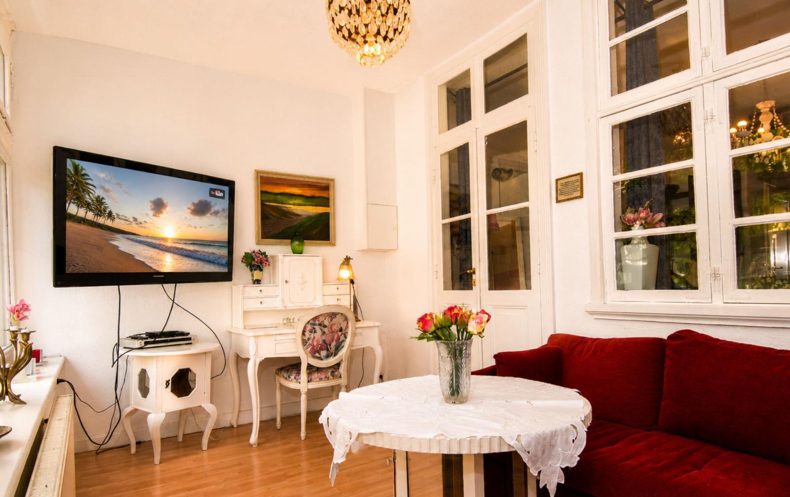Ein Wohnzimmer mit rotem Sofa, weißem Schreibtisch und Fernseher an der Wand.
