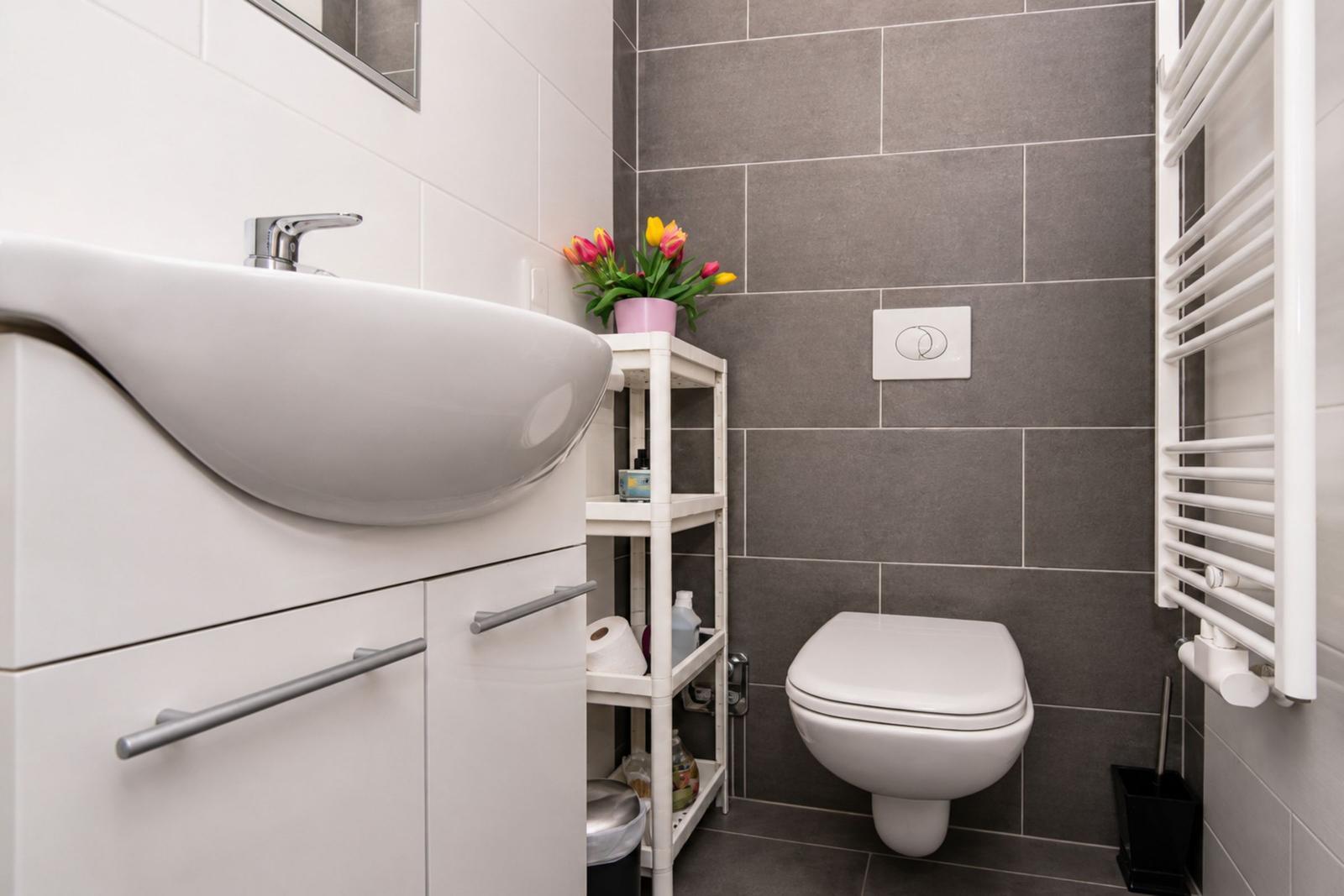 Bad mit Waschbecken, Toilette und Heizkörper an der Wand.