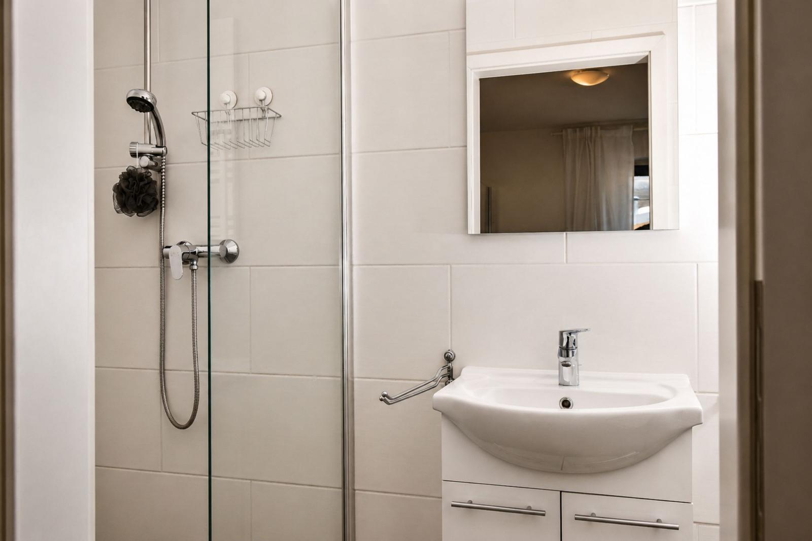 Dusche mit Glaswand, Waschbecken und Spiegel an der Wand.