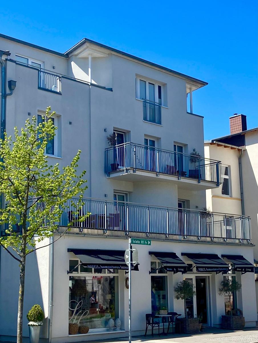 Haus mit Balkonen und Geschäften im Erdgeschoss unter blauem Himmel.