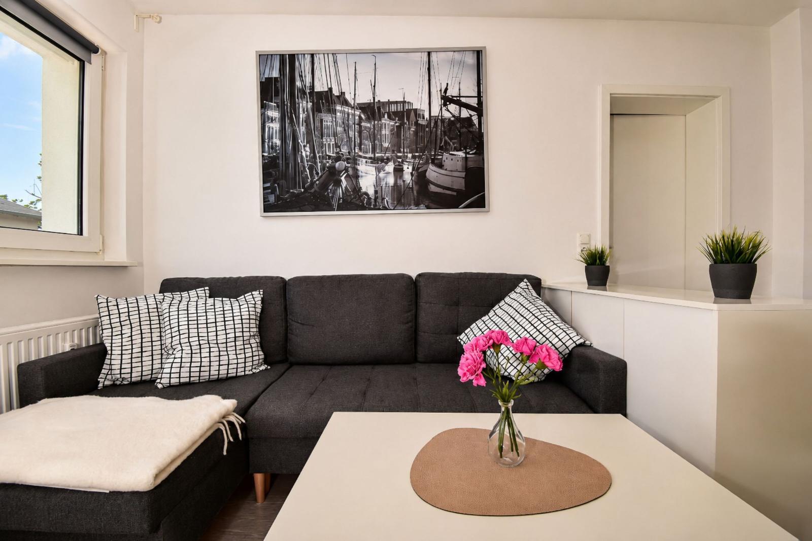 Ein Wohnzimmer mit grauem Sofa, weißen Kissen und einem Tisch mit rosa Blumen.