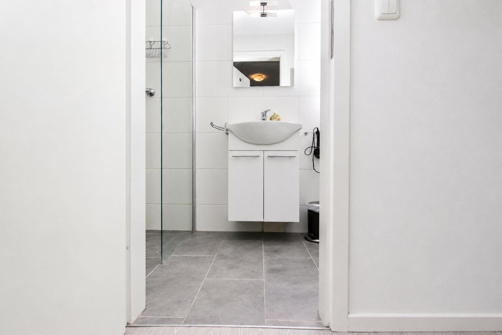 Badezimmer mit Dusche, Waschbecken und Spiegel.