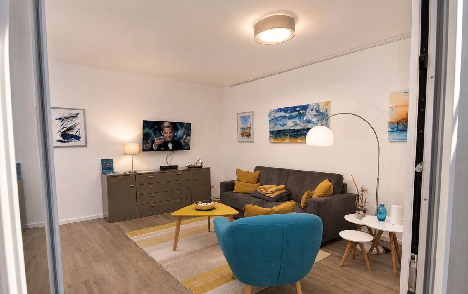 Wohnzimmer mit Sofa, blauer Sessel und Fernseher an der Wand.