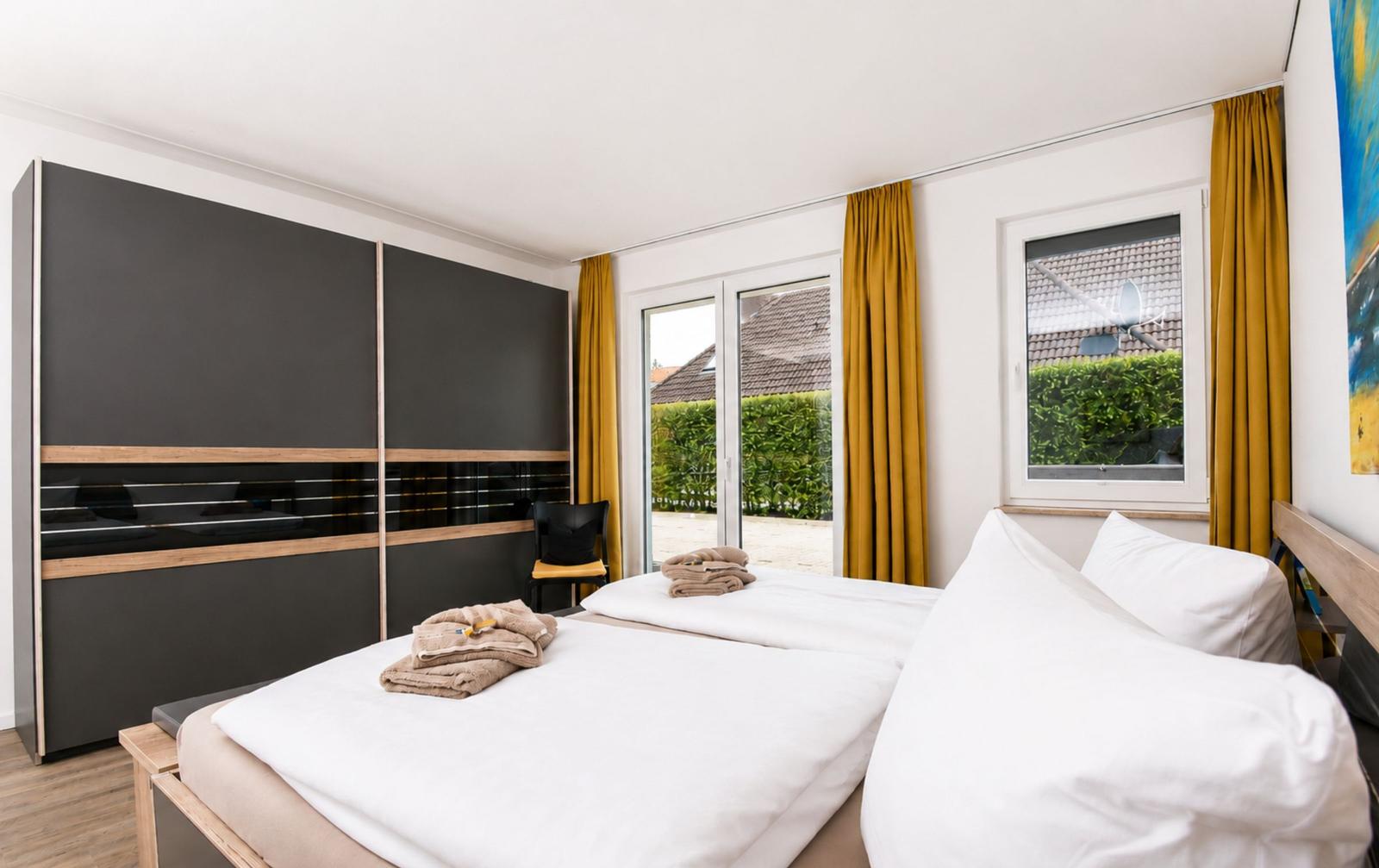 Schlafzimmer mit Doppelbett, Schrank und Fenster zur Außenterrasse.