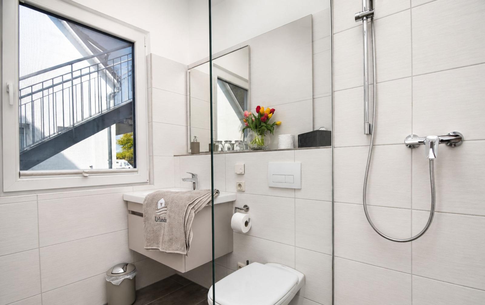 Badezimmer mit Dusche, Waschbecken und Toilette. Fenster mit Blick auf Balkon.