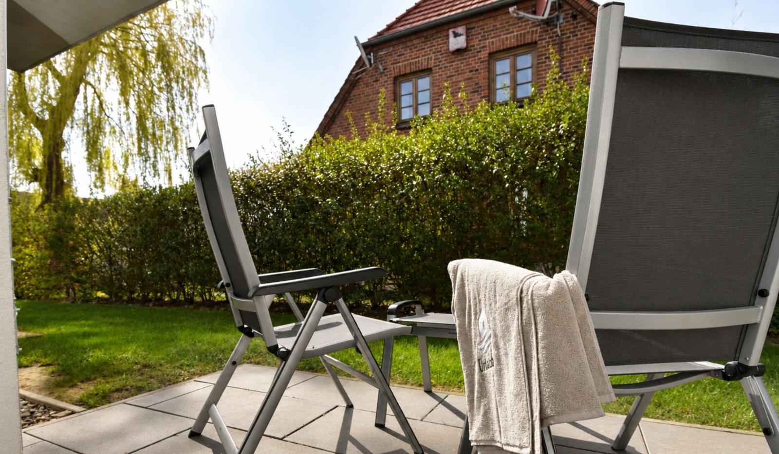 Zwei Liegestühle auf Terrasse mit Blick auf grünen Garten und Backsteinhaus.