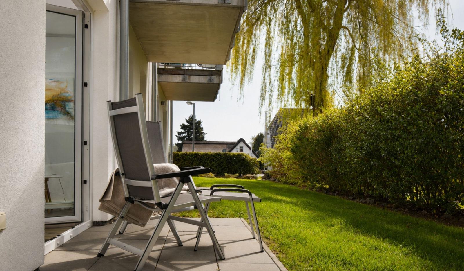 Terrasse mit Liegestuhl und Blick auf grünen Rasen und Weidebaum.