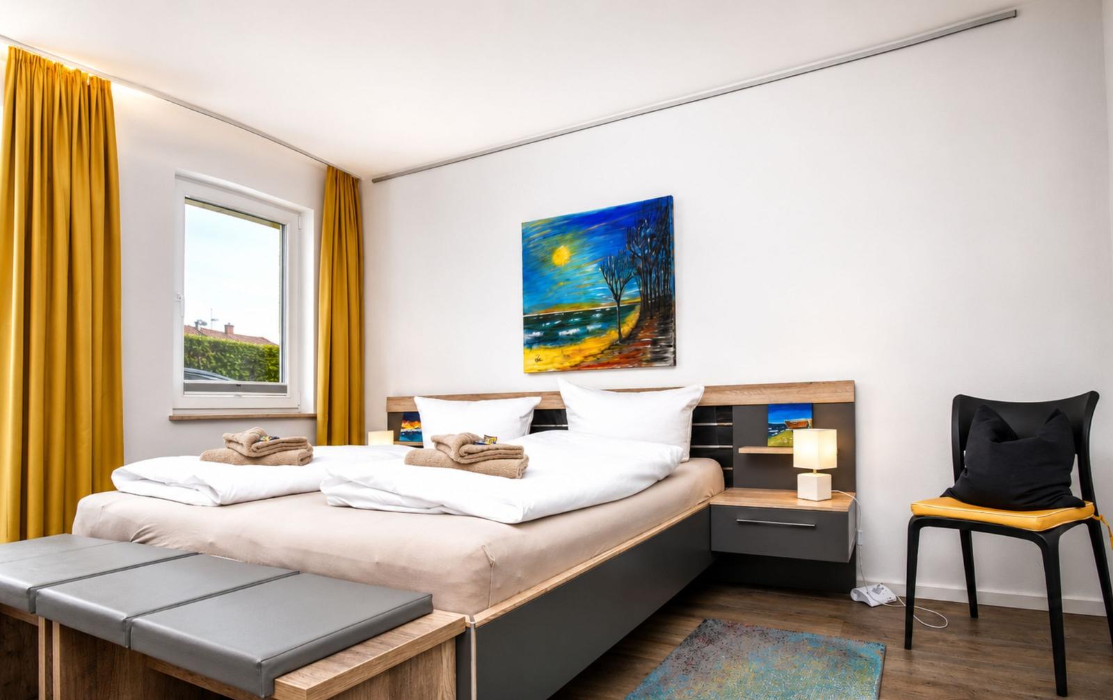 Schlafzimmer mit Bett, Fenster, Vorhängen und Wandbild.