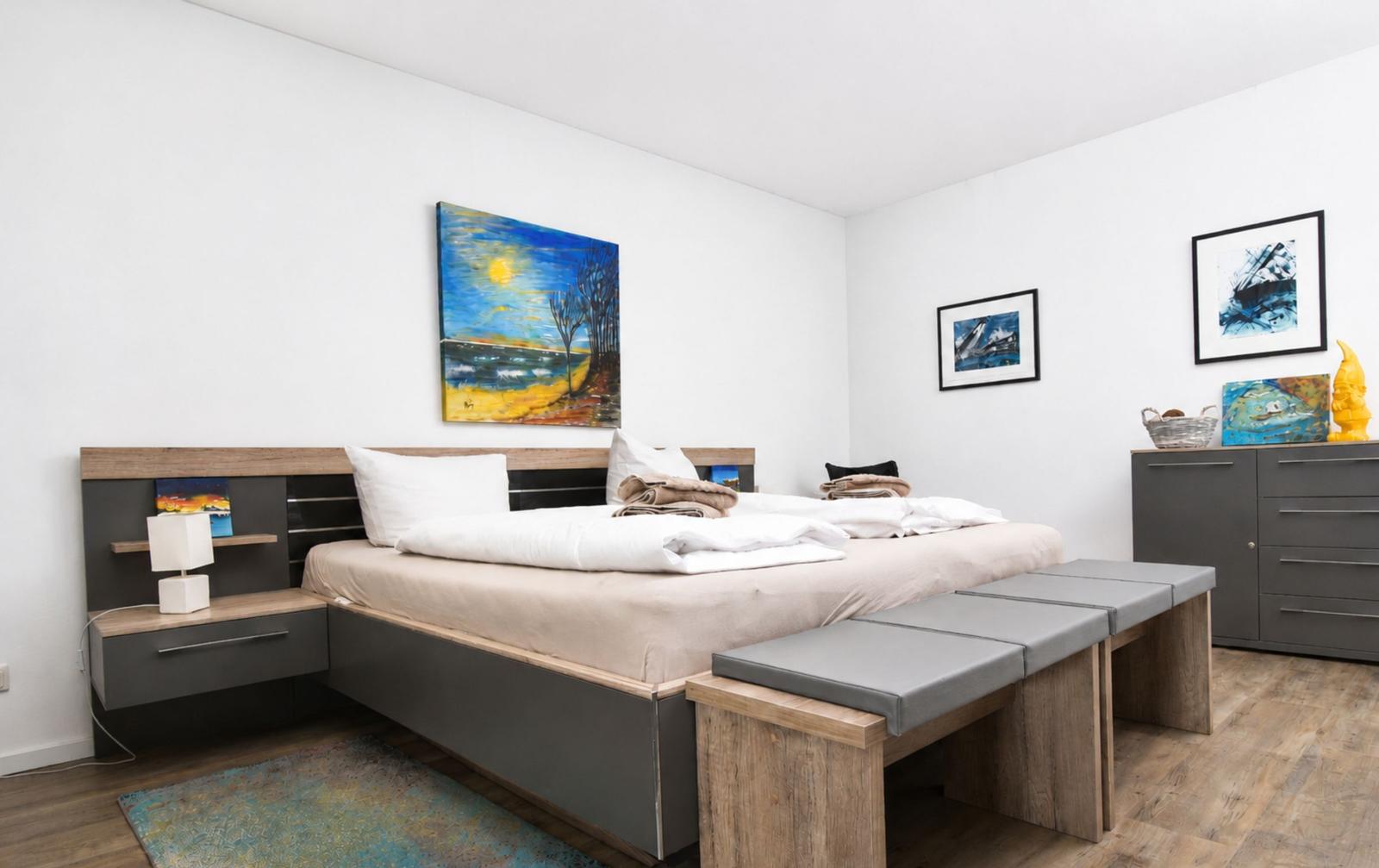 Schlafzimmer mit Bett, Nachttisch und Wandbildern.