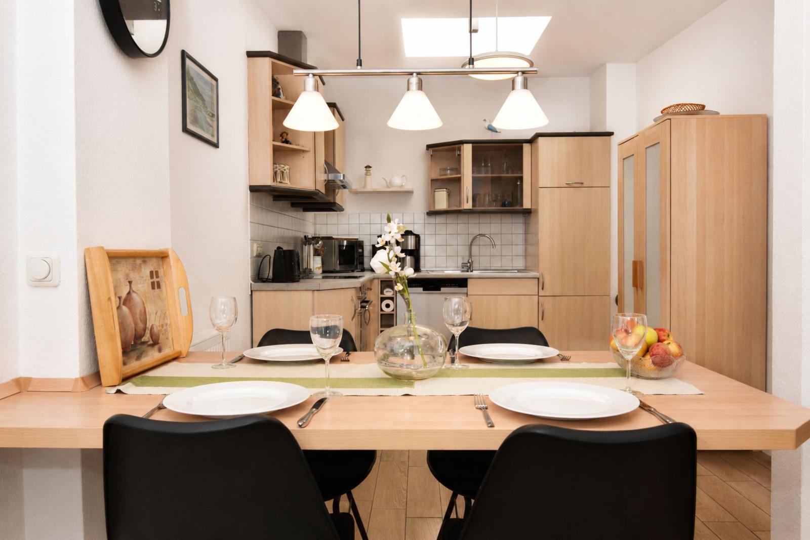 Essbereich mit Tisch, Stühlen und gedecktem Tisch. Küche im Hintergrund mit Holzmöbeln.