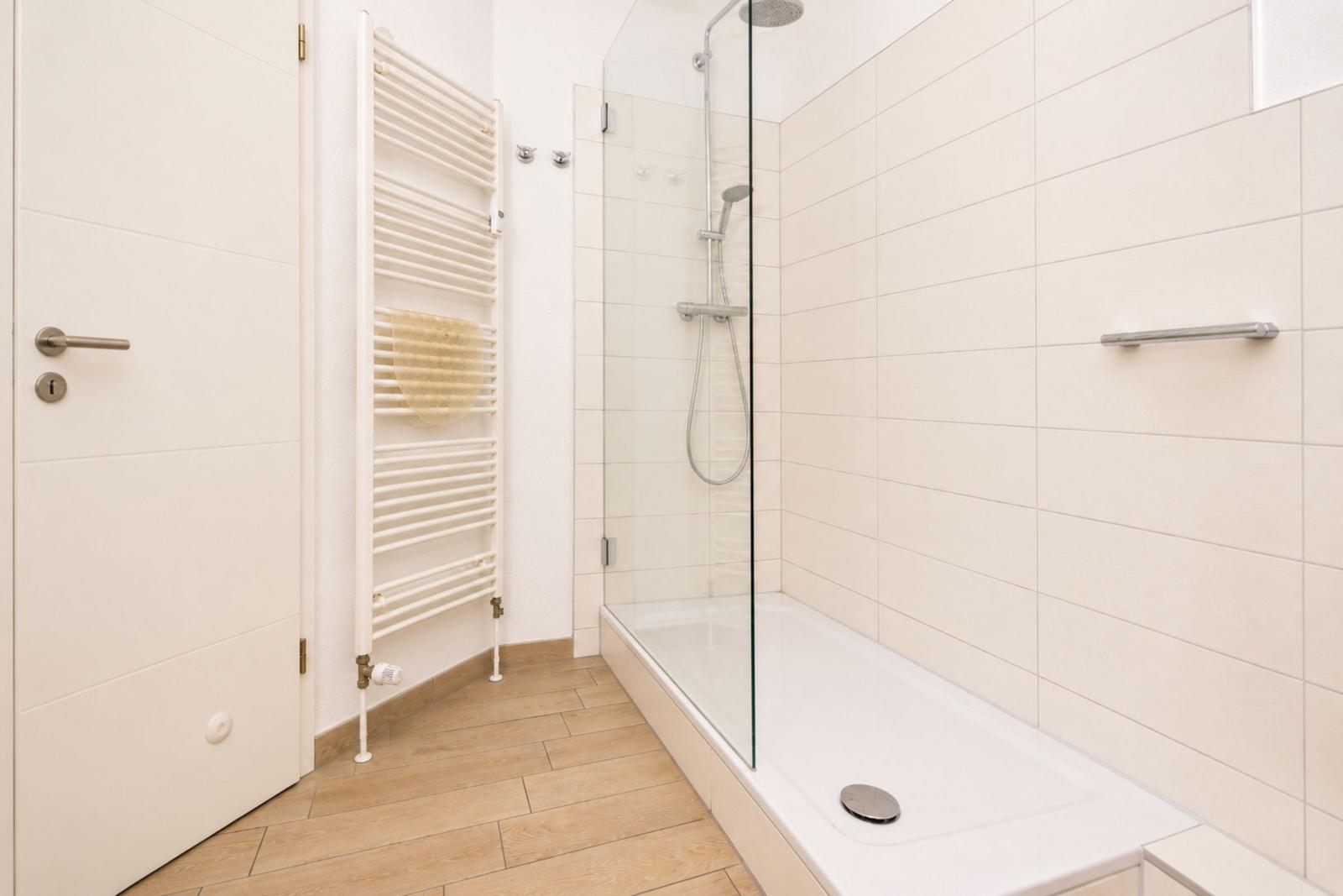 Badezimmer mit Dusche, Heizkörper und Holzfußboden.