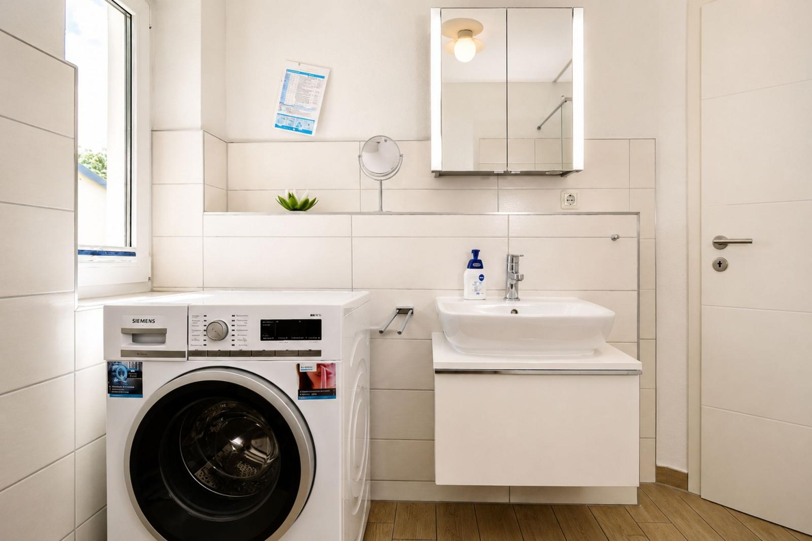 Badezimmer mit Waschmaschine, Waschbecken und Spiegelschrank.