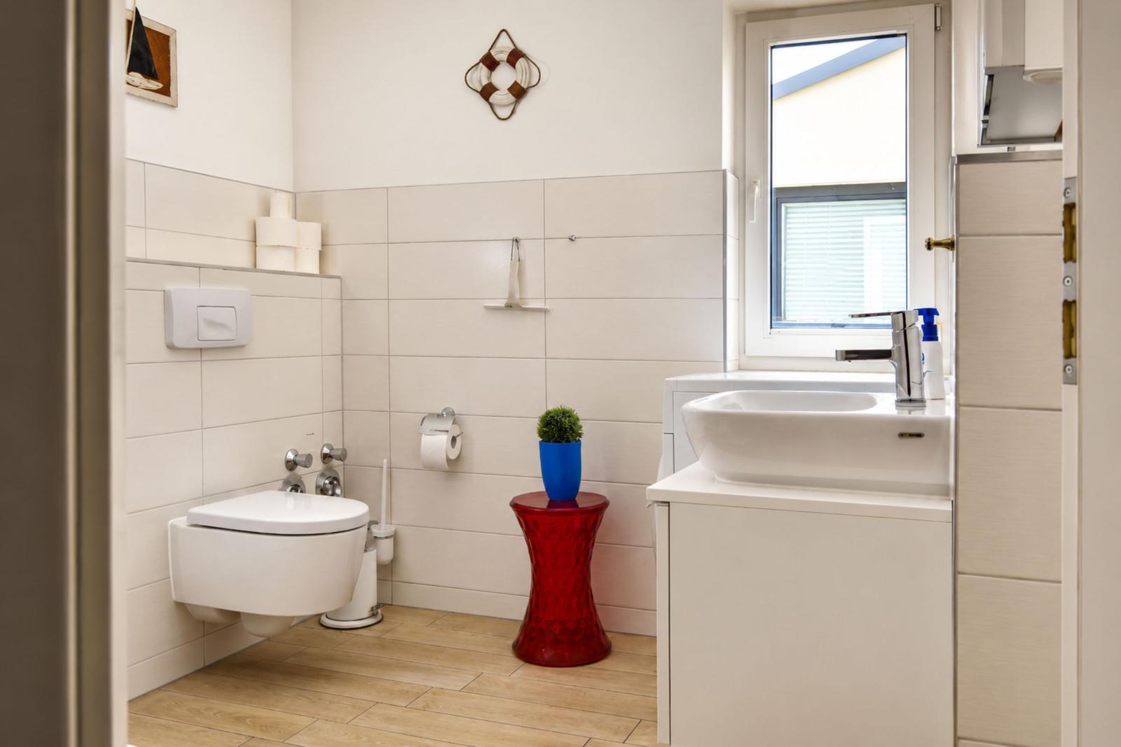 Badezimmer mit Toilette, Waschbecken und rotem Beistelltisch.