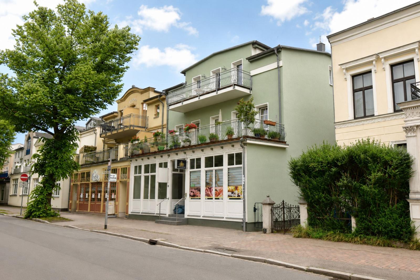 Grün gestrichenes Gebäude mit Balkonen und Pflanzen an der Fassade.