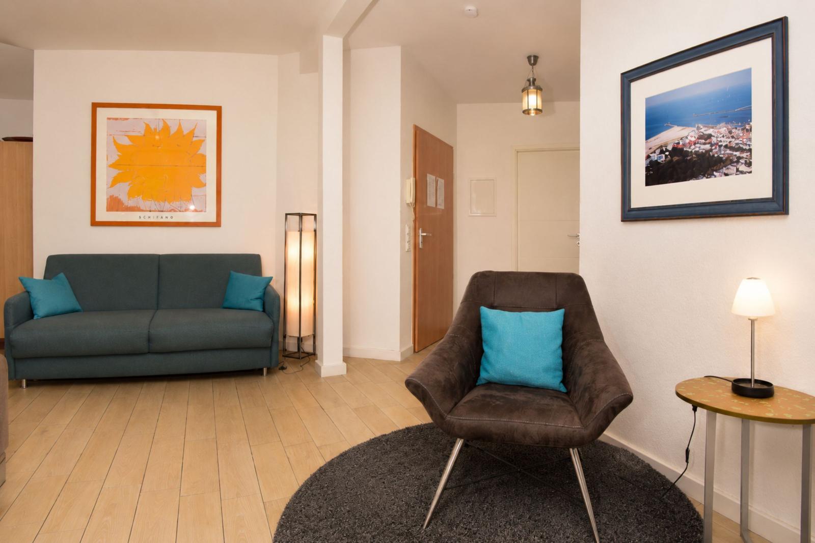 Wohnzimmer mit Sofa, Sessel und Wandbildern.