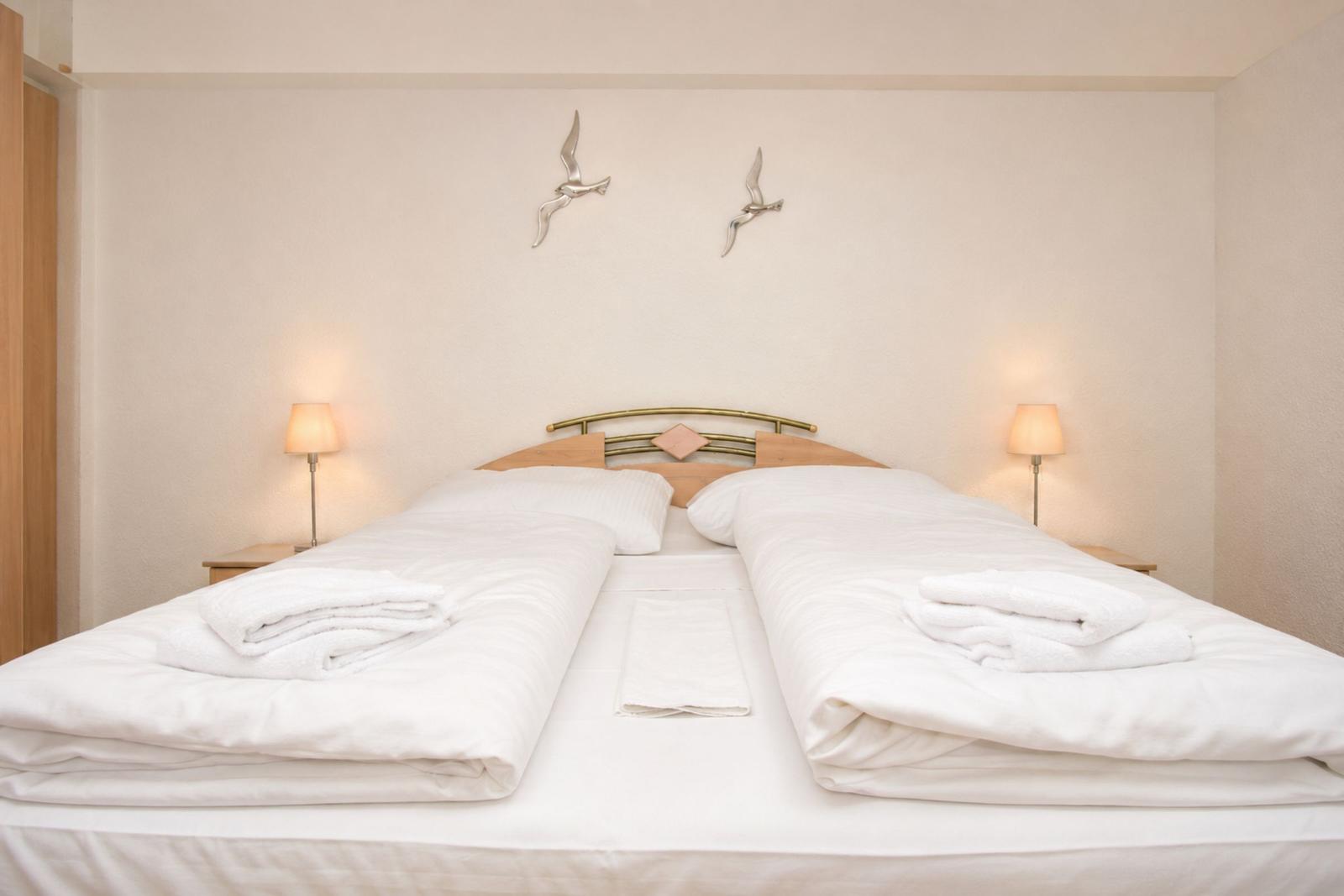 Zimmer mit Doppelbett, zwei Nachttischen und Wanddekoration mit Vögeln.