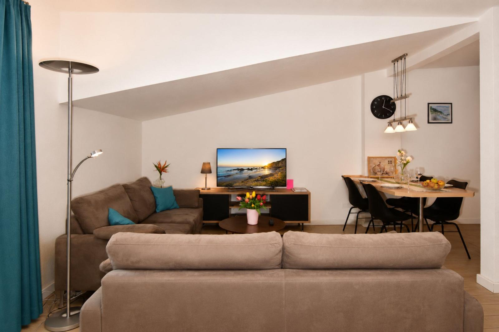 Wohn- und Essbereich mit Sofa, Fernseher und Esstisch mit Stühlen.