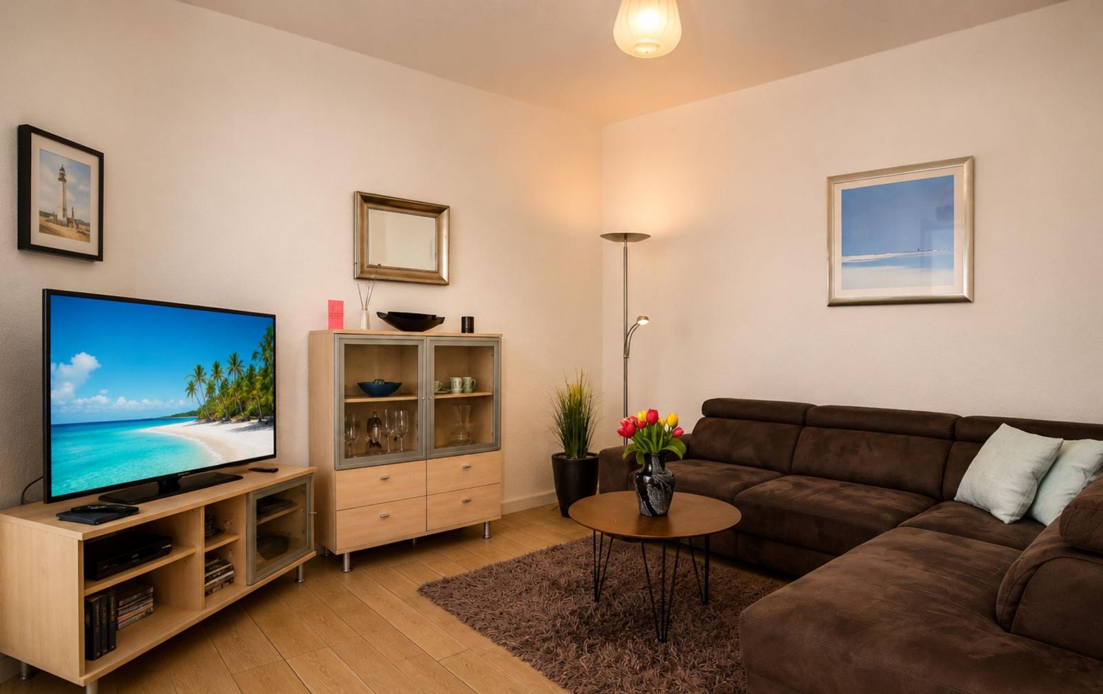 Wohnzimmer mit Sofa, Fernseher und Glaswand-Schrank. Holzboden und Teppich.