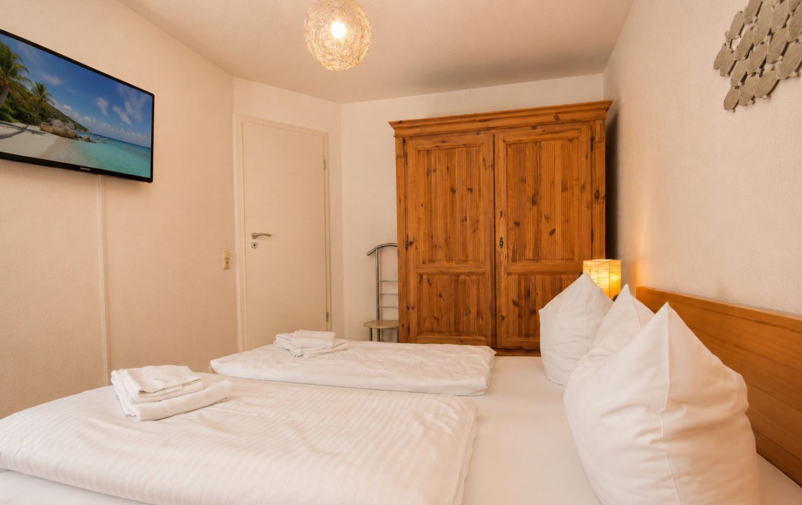 Zimmer mit Doppelbett, Holzschrank und Wand-TV mit Strandbild.
