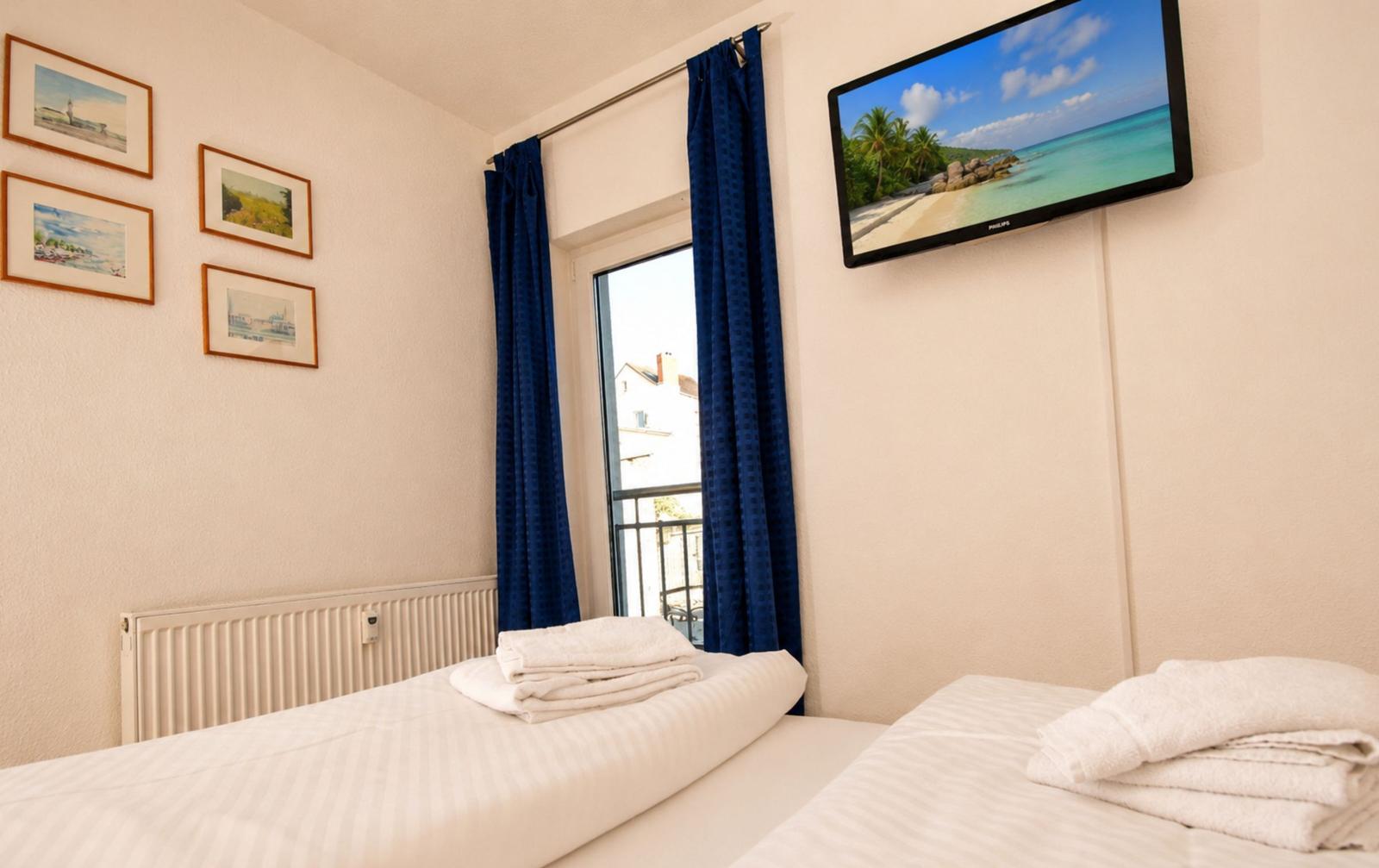 Zwei Betten mit weißen Bettwäsche, TV und Fenster mit blauen Vorhängen.