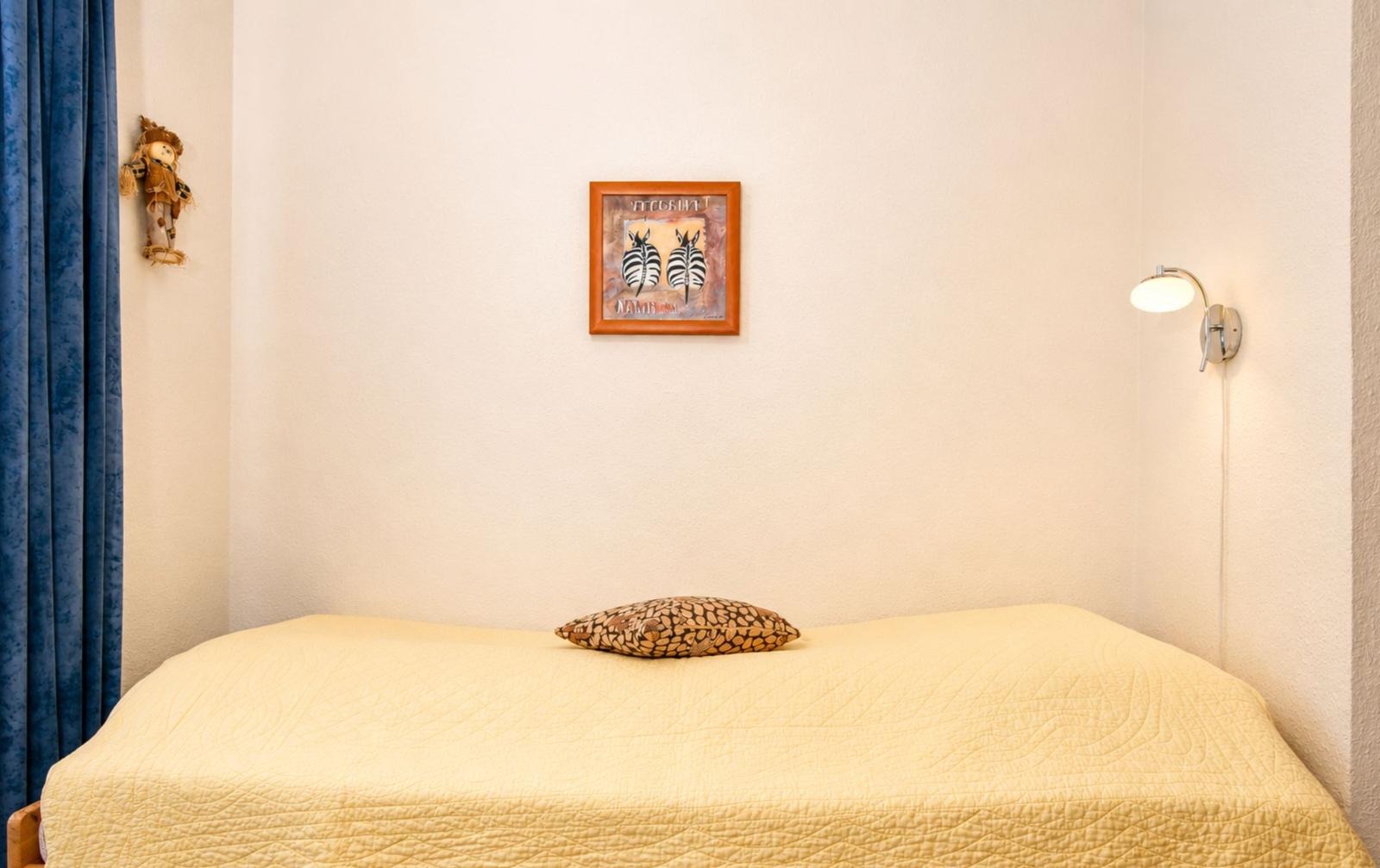 Ein Bett mit gelber Bettdecke und Kissen. Wandbild mit Zebras und Wandlampe.