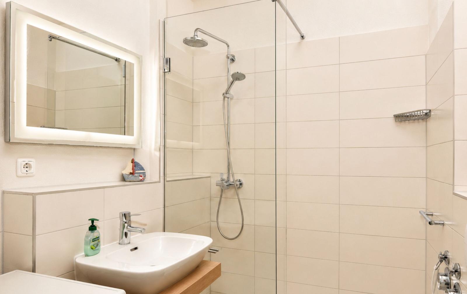 Badezimmer mit Dusche, Waschbecken und beleuchtetem Spiegel