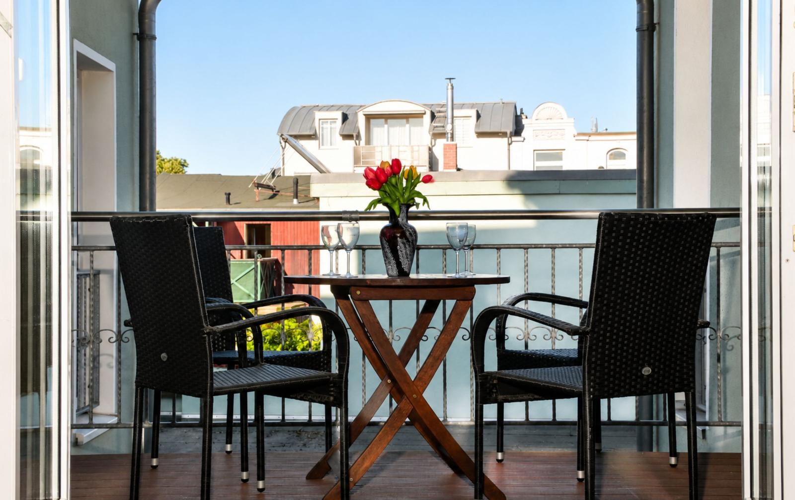 Terrasse mit Tisch, zwei Stühlen und Blumenarrangement. Blick auf benachbarte Gebäude.