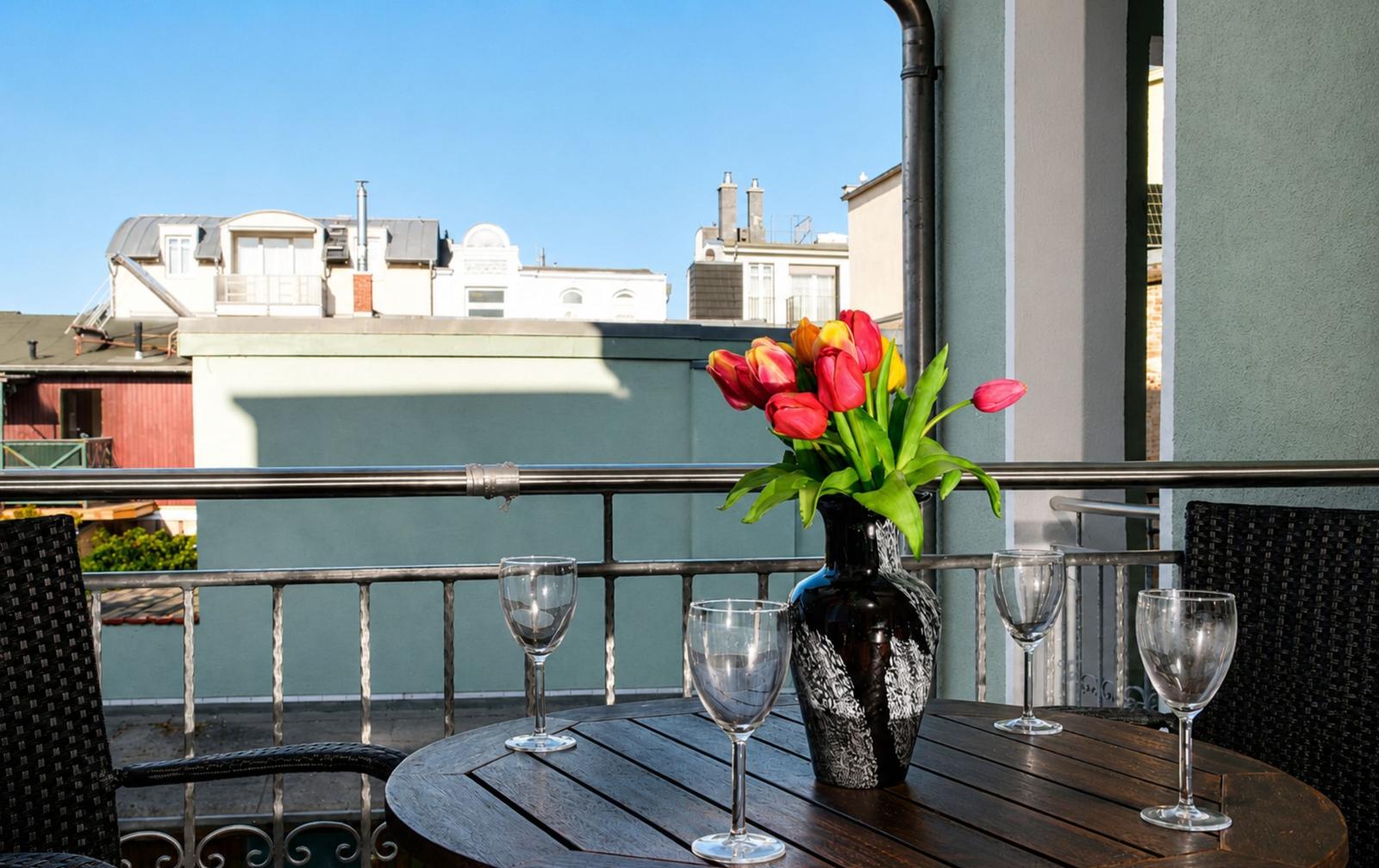Terrasse mit Tisch, Stühlen und Blumen. Blick auf Gebäude im Hintergrund.