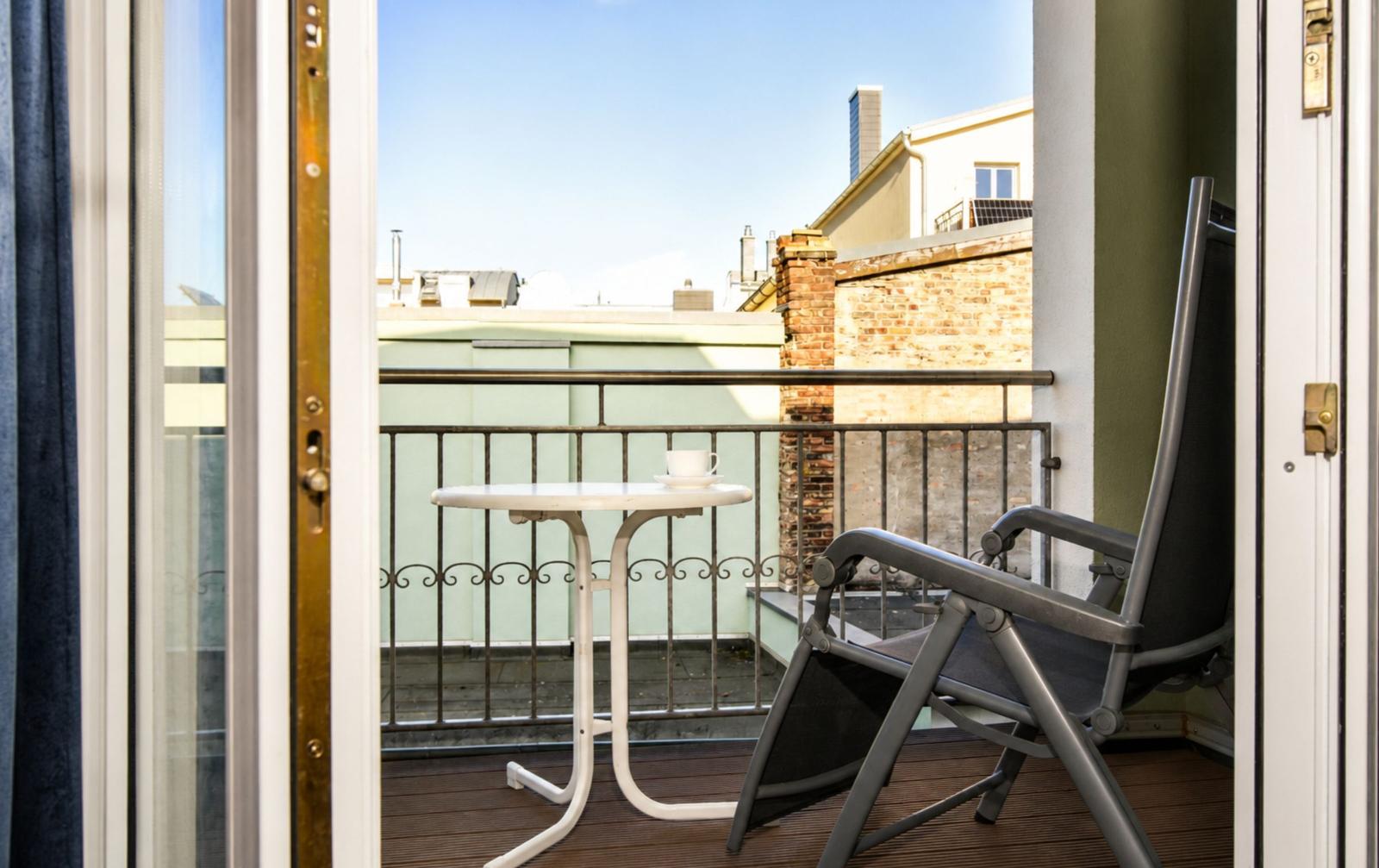 Balcony with table, cup, and chair. View of rooftops and brick wall.