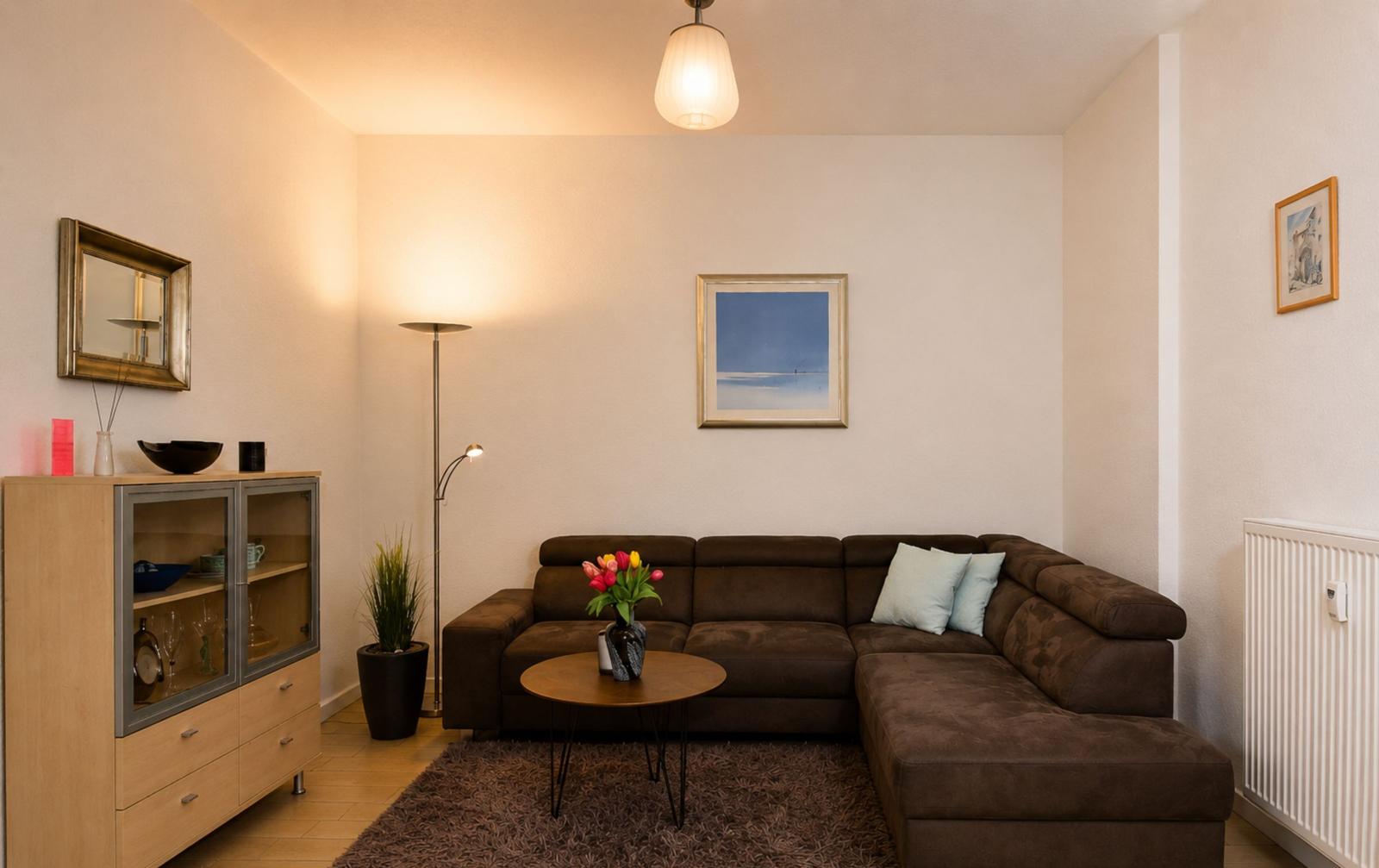 Wohnzimmer mit braunem Sofa, runden Tisch und Beleuchtung.