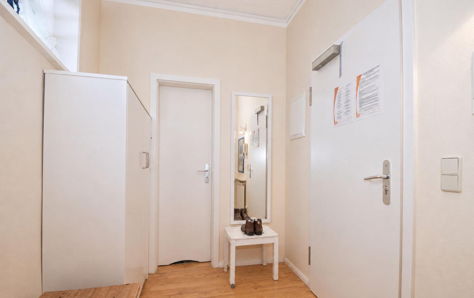 Eingangsbereich mit Kleiderschrank, Spiegel und Tür. Holzboden und weiße Wände.