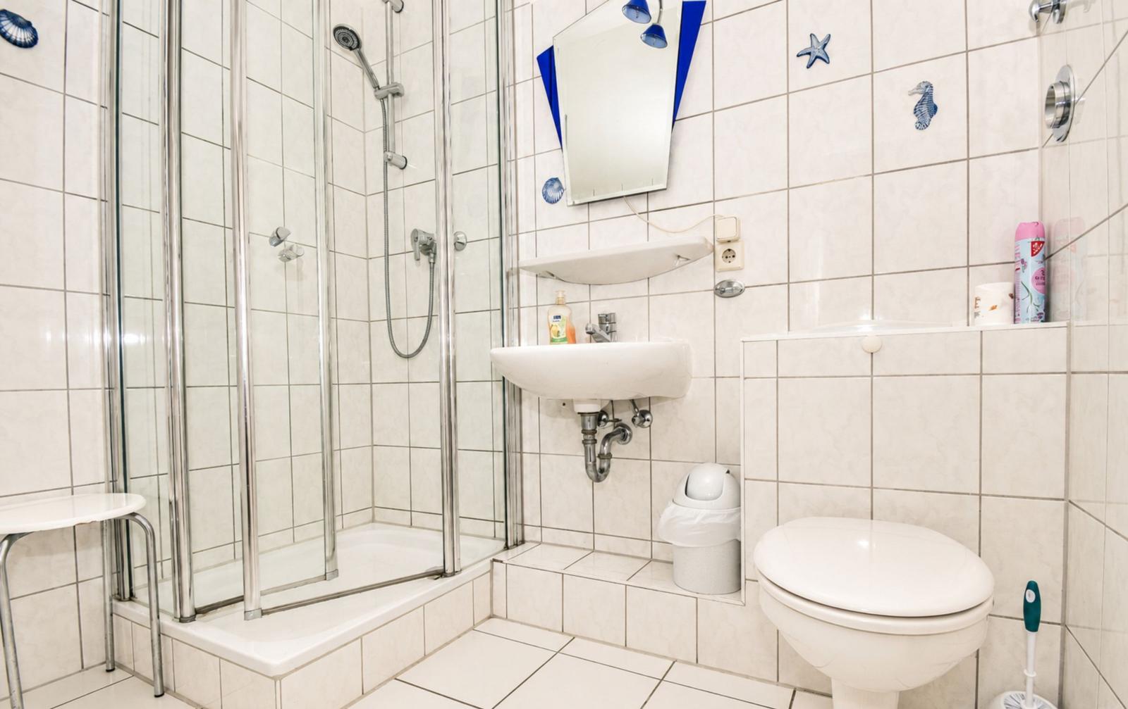 Badezimmer mit Dusche, Waschbecken und Toilette. Wandfliesen und Meeresmotiv-Dekoration.