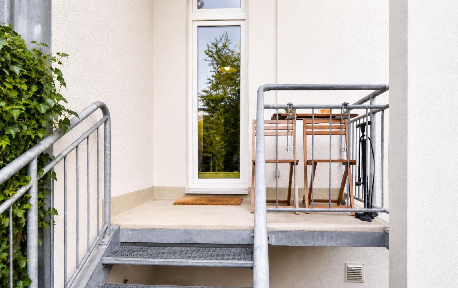 Terrasse mit Tisch, zwei Stühlen und Stufen zur Eingangstür.