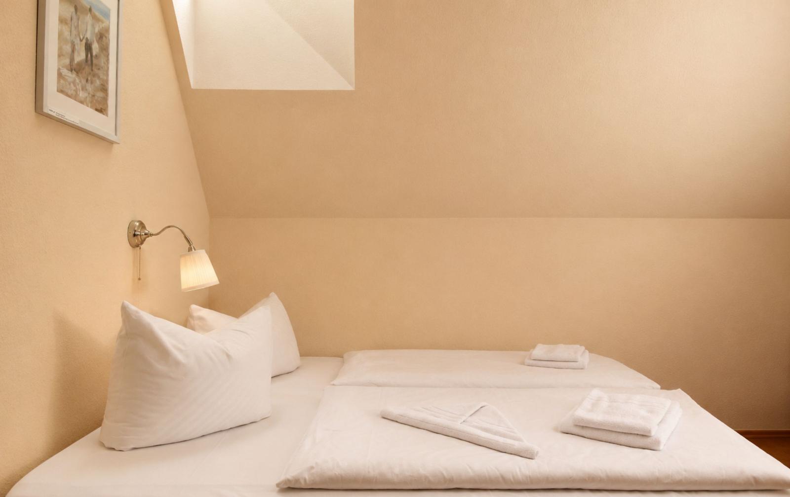 Doppelbett mit weißen Kissen und Handtüchern unter einem Dachbodenfenster.