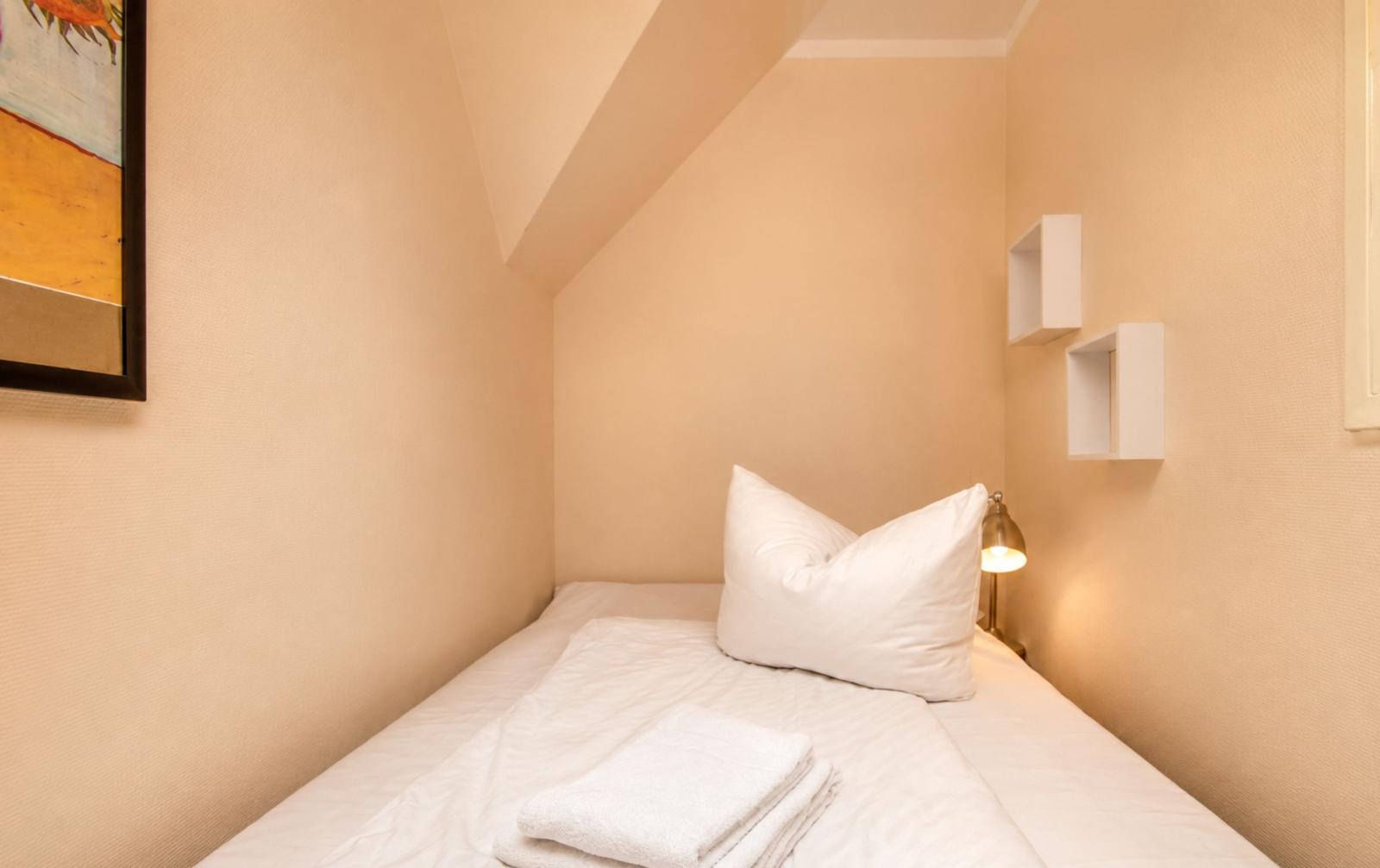 Schlafzimmer mit Bett, Kissen und Handtuch unter schrägen Dachbodenwänden.