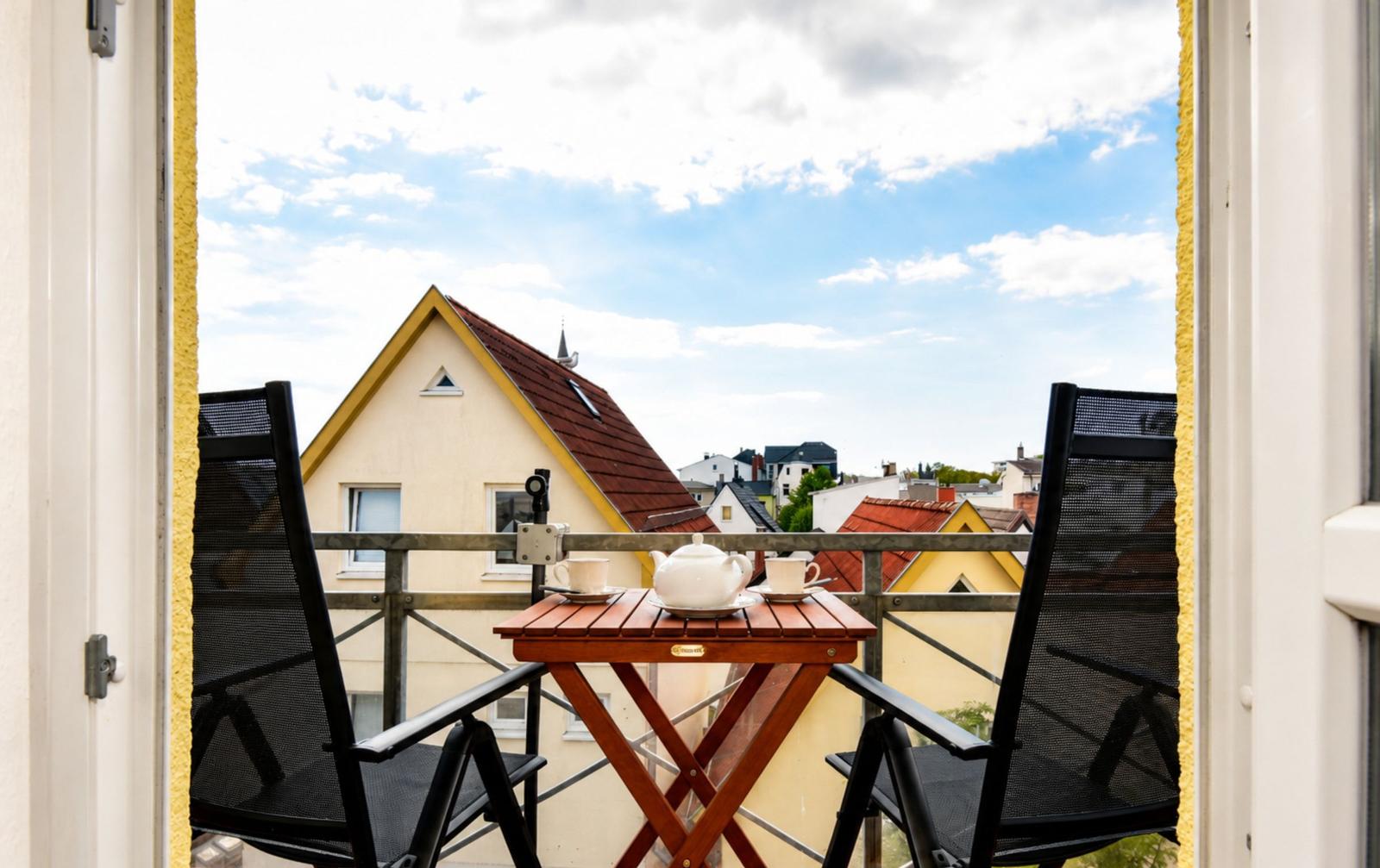Balcony with table and chairs, view of rooftops and sky.