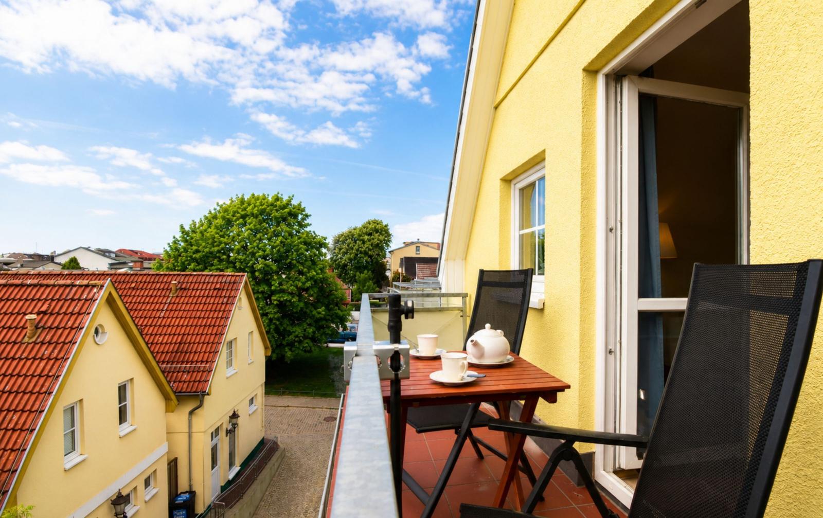 Terrasse mit Tisch und Stühlen, Blick auf gelbe Häuser und Bäume.