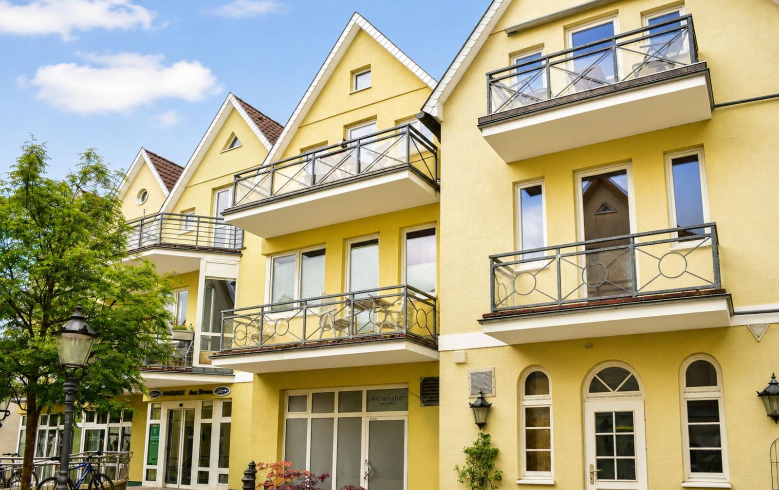 Gelbes Mehrfamilienhaus mit Balkonen und Fenstern unter blauem Himmel.