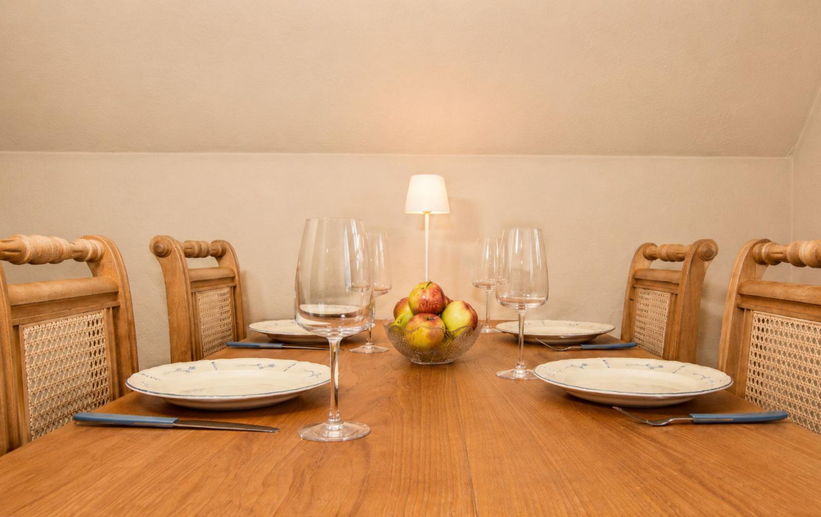 Holztisch mit vier Stühlen, Teller, Gläsern und Obstschale.