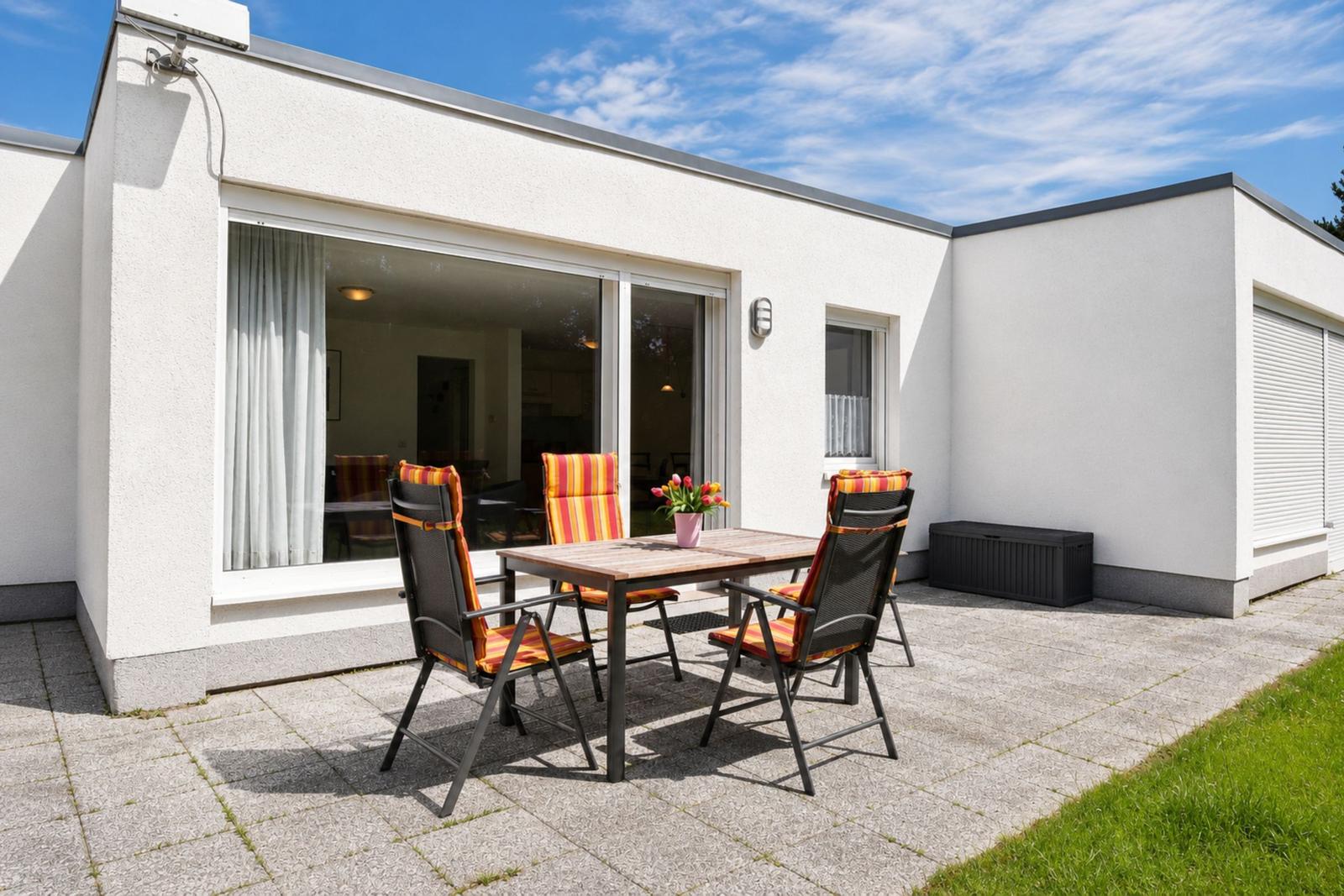 Terrasse mit Tisch und Stühlen vor modernem Haus mit Glasfront.