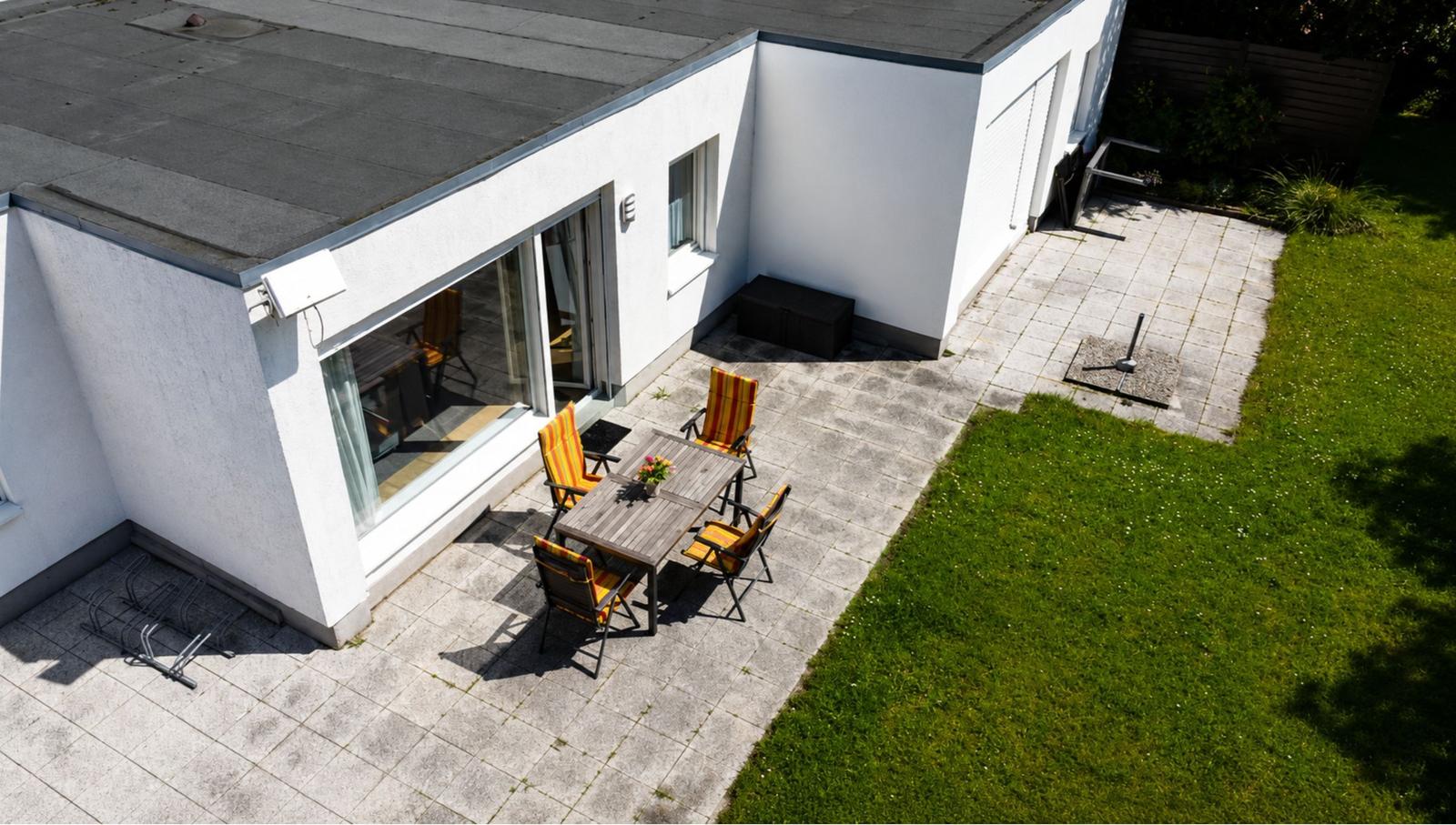 Terrasse mit Tisch und Stühlen neben einem weißen Haus mit grünem Garten.