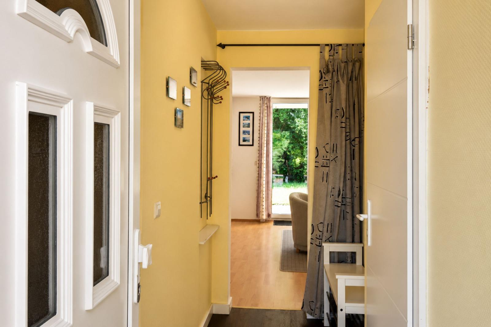 Hausgang mit gelben Wänden, Garderobe und Blick ins Wohnzimmer mit Fenster.