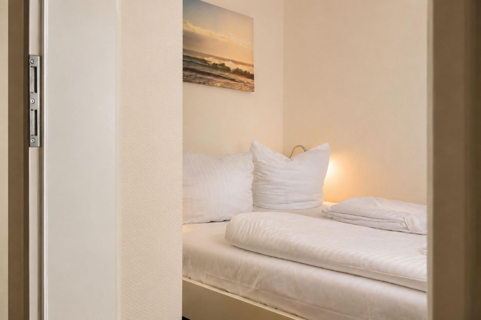 Schlafzimmer mit weißem Bett, zwei Kissen und Wandbild an der Wand.