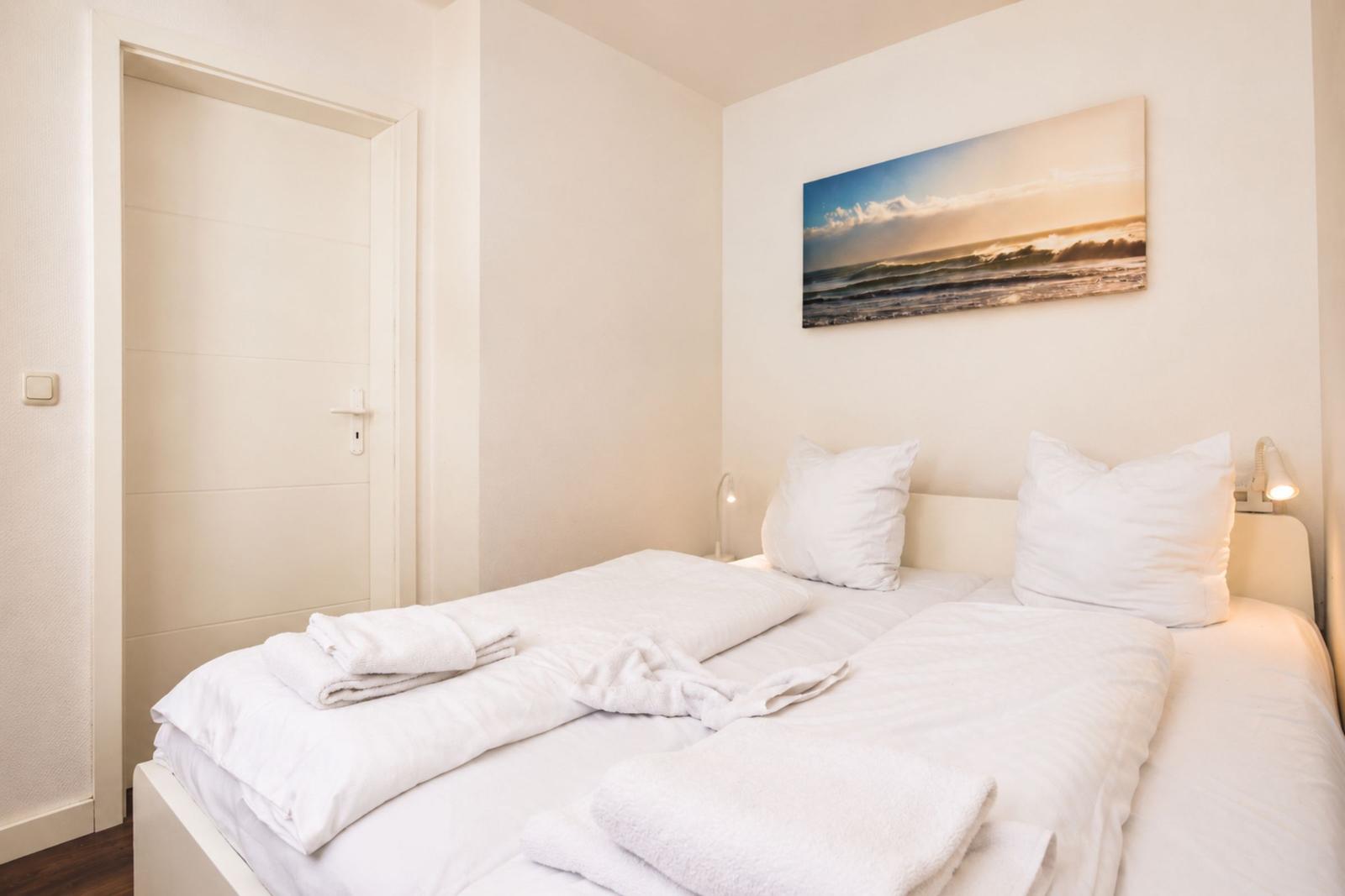 Schlafzimmer mit Bett, weißen Kissen und Strandbild an der Wand.