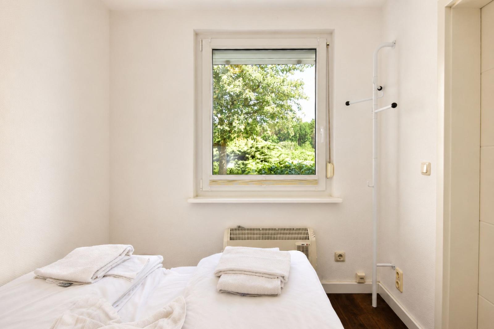 Ein Schlafzimmer mit Bett, Fenster und Kleiderständer.