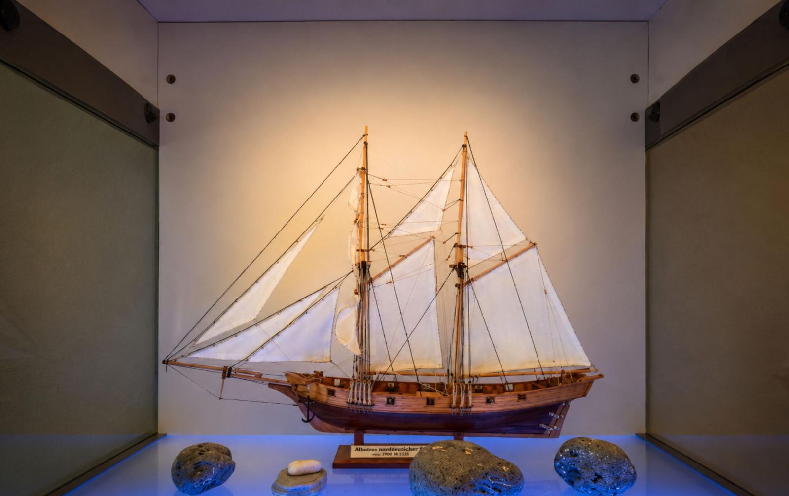 A model of a sailing ship with white sails and wooden structure on a base.