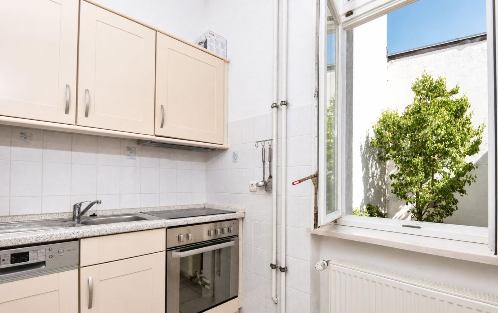 Küche mit hellen Schränken, Spüle und Fensterblick auf einen Baum.