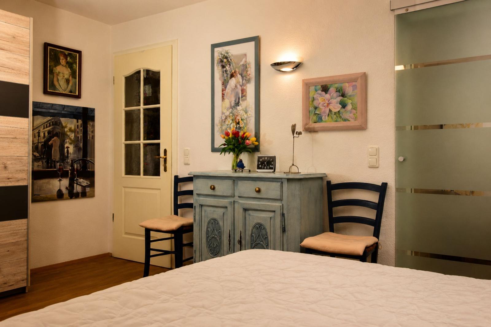 Bedroom with bed, wardrobe, table and chairs, wall art, and a door.