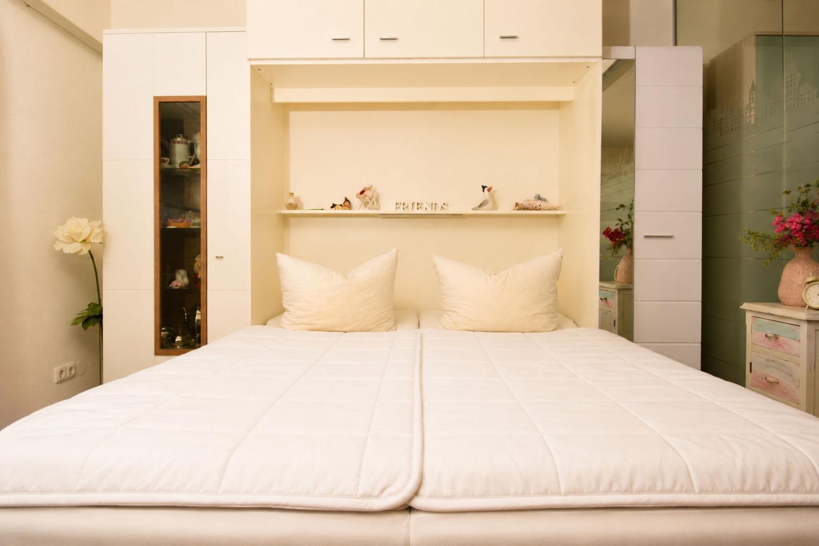 A bed with white bedding and two pillows. Behind the bed is a shelf with decor.